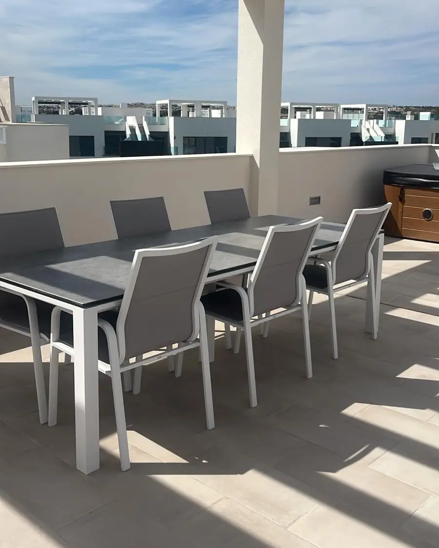 Een lange eettafel met stoelen onder de witte pergola op het dakterras